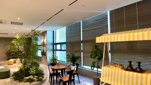 Un espacio interior moderno con una mesa redonda y sillas, plantas en macetas y un mantel a rayas amarillas.