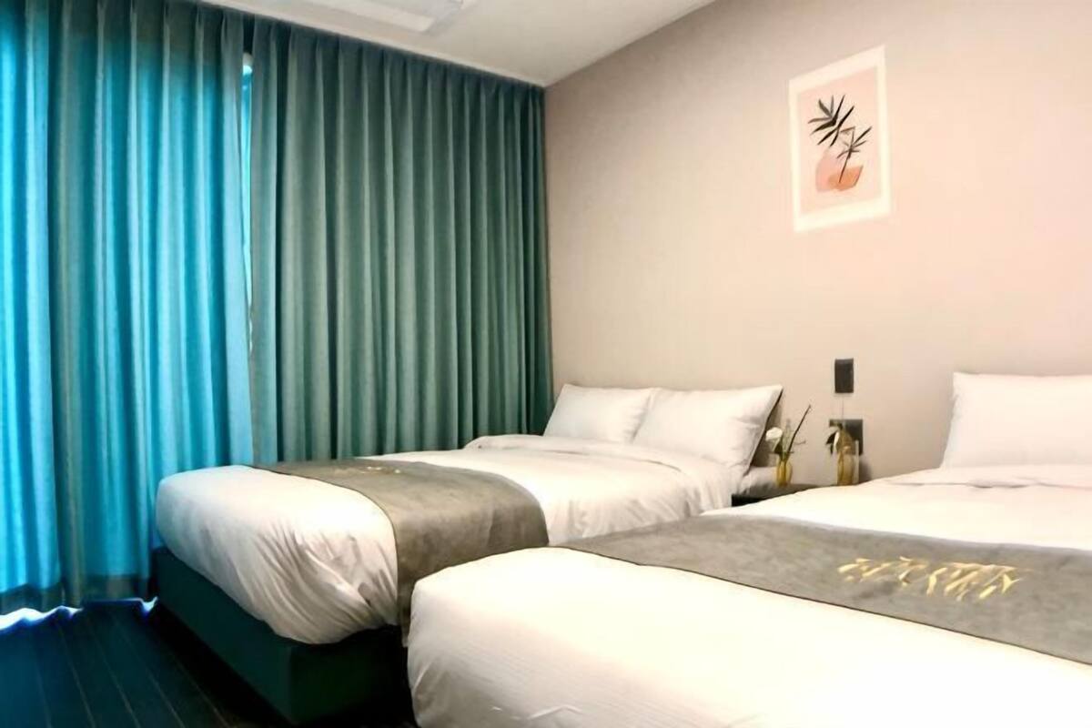 Una habitación de hotel con dos camas, un ventanal con cortinas, una obra de arte en la pared y una mesita de noche con un florero.
