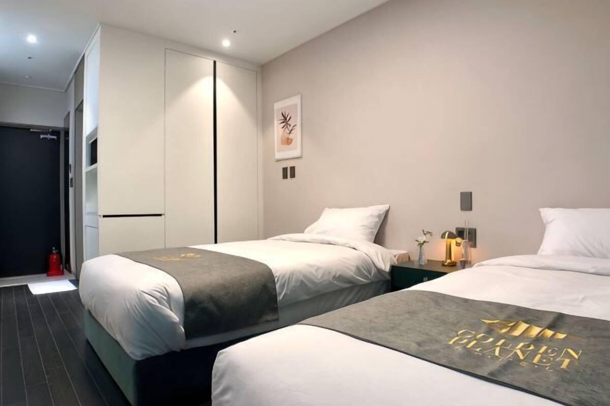 Habitación de hotel con dos camas, un armario, una mesita con una lámpara y una obra de arte colgada en la pared.