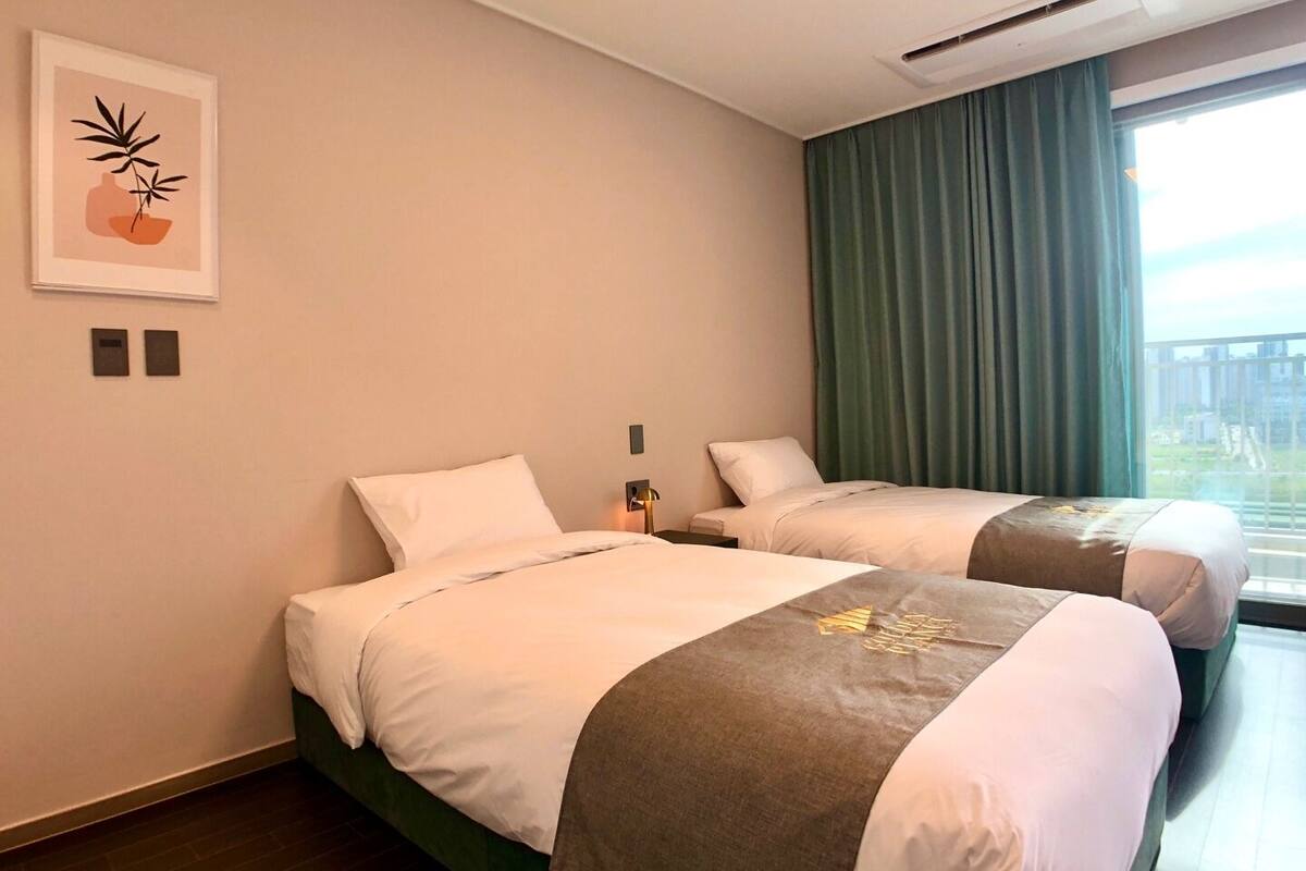 Una habitación de hotel con dos camas, una cortina verde y un cuadro enmarcado en la pared.