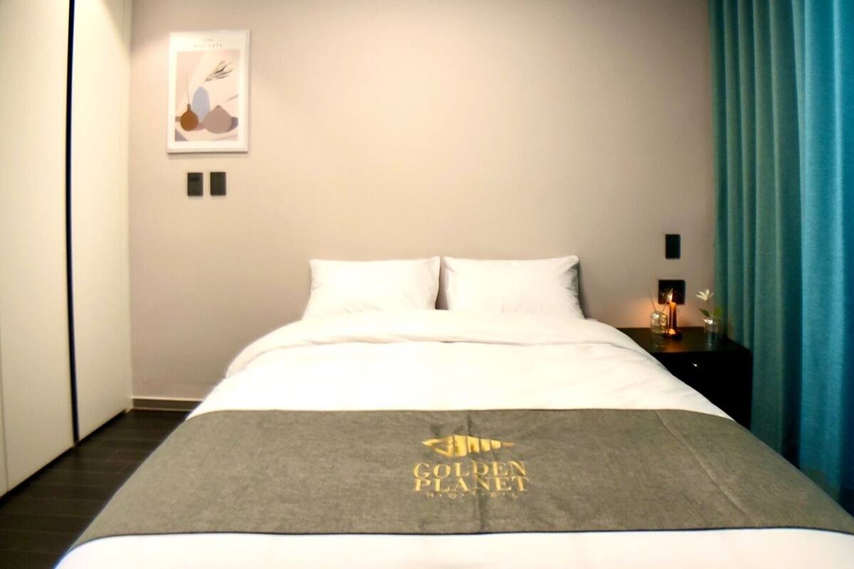 Habitación de hotel con cama, mesita de noche, un cuadro enmarcado en la pared y una cortina azul.