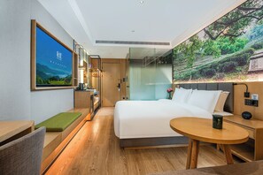 A modern hotel room with a large bed, a small round table, a desk with a chair, a shower area, and a large window with a scenic view. - True Go Hotel Nanshan  (Shenzhen)