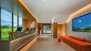 Un moderno vestíbulo de hotel con mostrador de recepción, zona de estar y una gran pantalla de televisión mostrando un paisaje pintoresco.