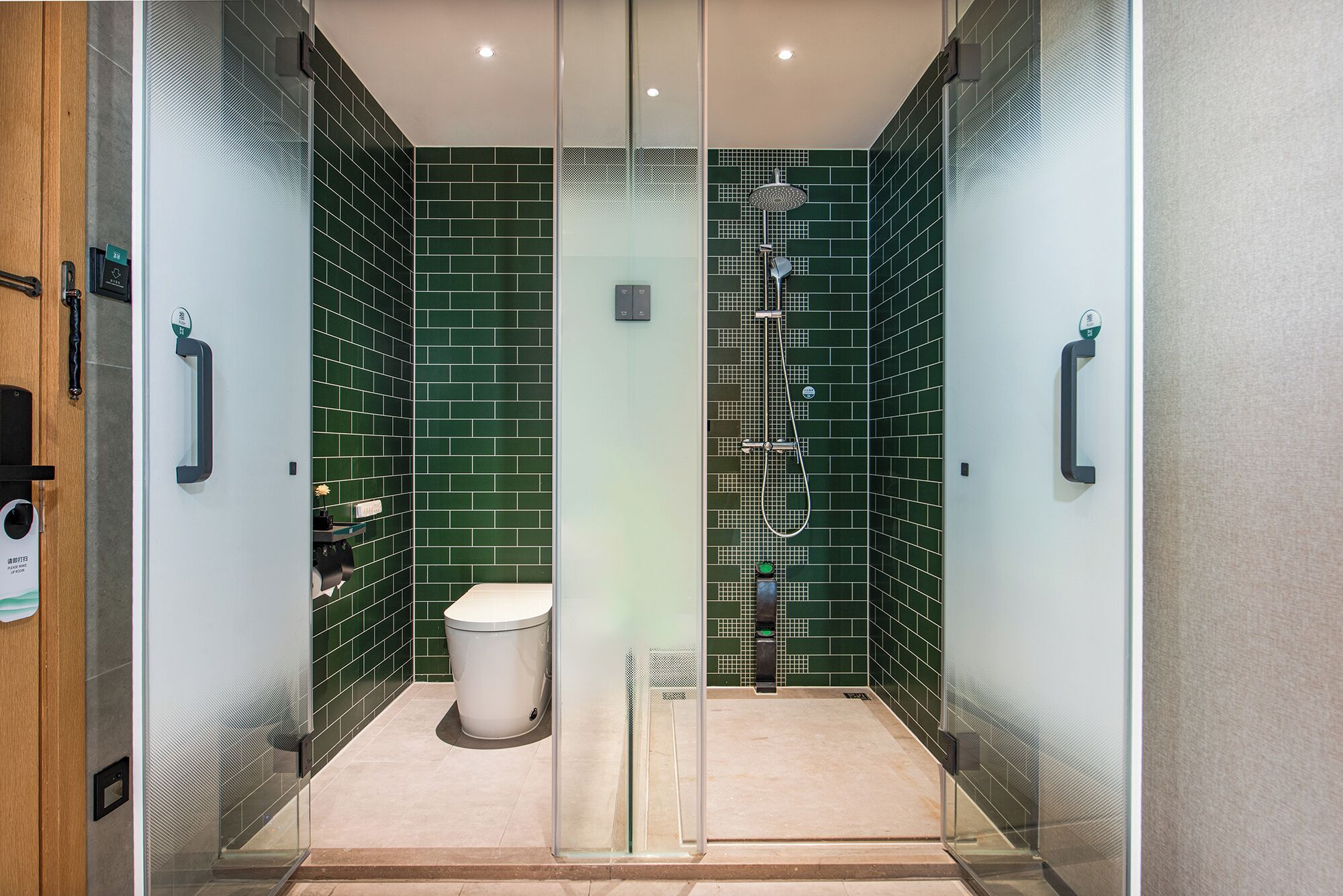 A modern bathroom with green-tiled walls, a glass-enclosed shower, and a white toilet.