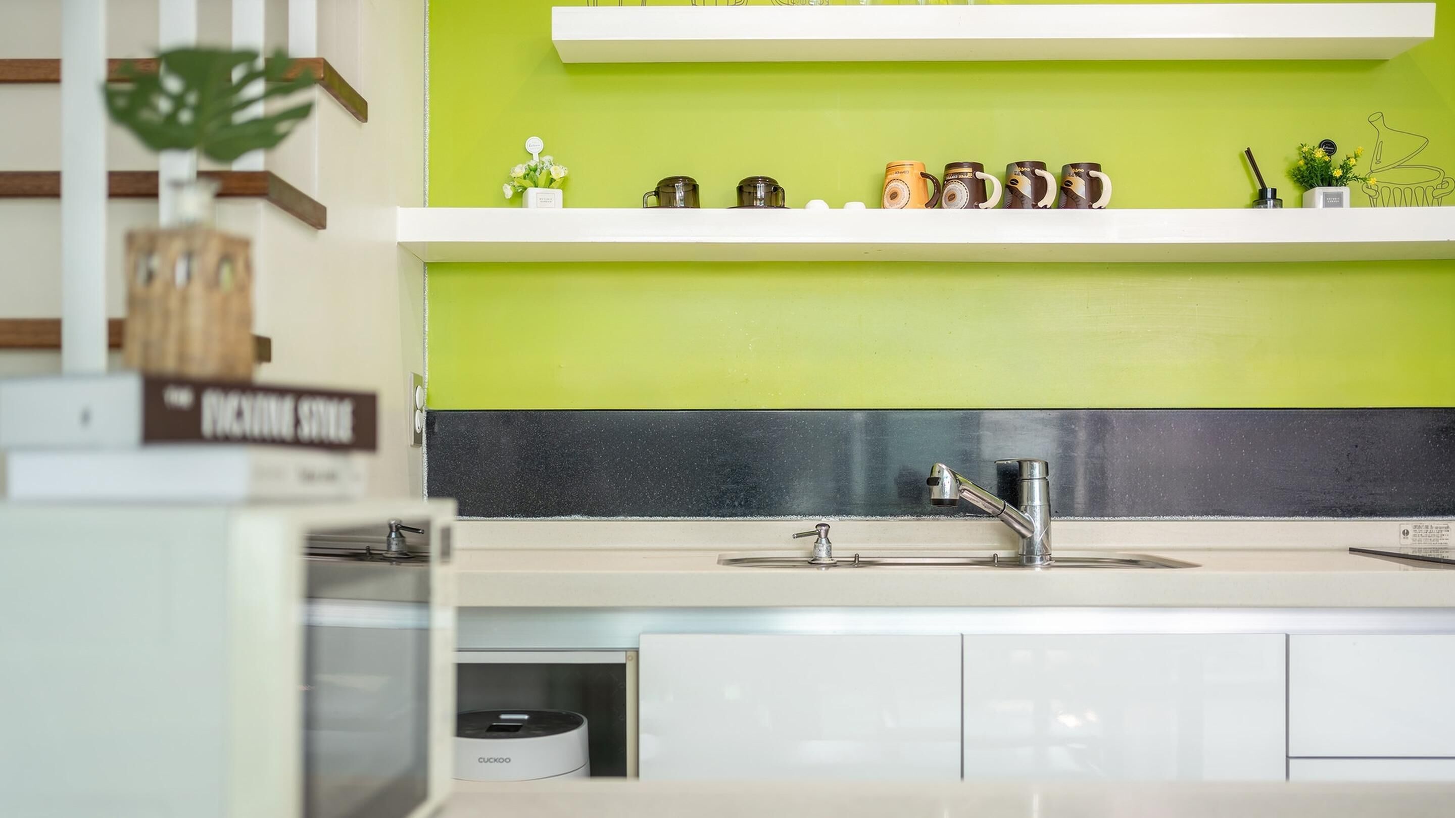 A modern kitchen with a green backsplash, a sink with a single faucet, and a countertop with a coffee machine.