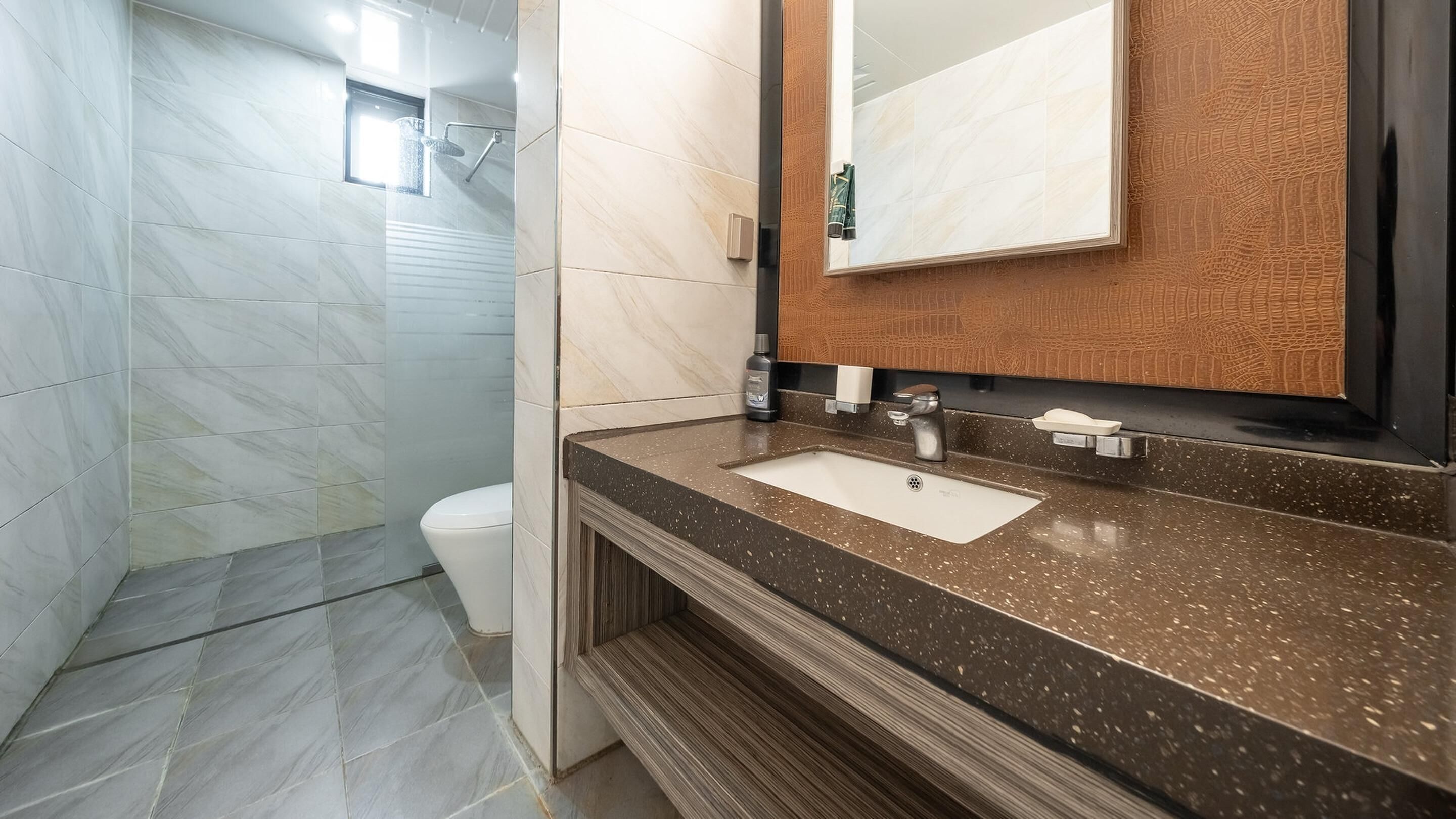 Een moderne badkamer met een marmeren douche, een wastafel met een gemarmerd aanrechtblad en een houten wastafelmeubel.