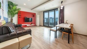 Un salón moderno con una pared de acento roja, un sofá de cuero, una mesa de comedor con sillas y un ventanal con vistas.