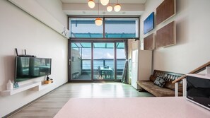 A modern living room with a large window, a flat-screen TV, a sofa, and a dining area with a table and chairs. - Sacheon Bichae Pension (Sacheon)