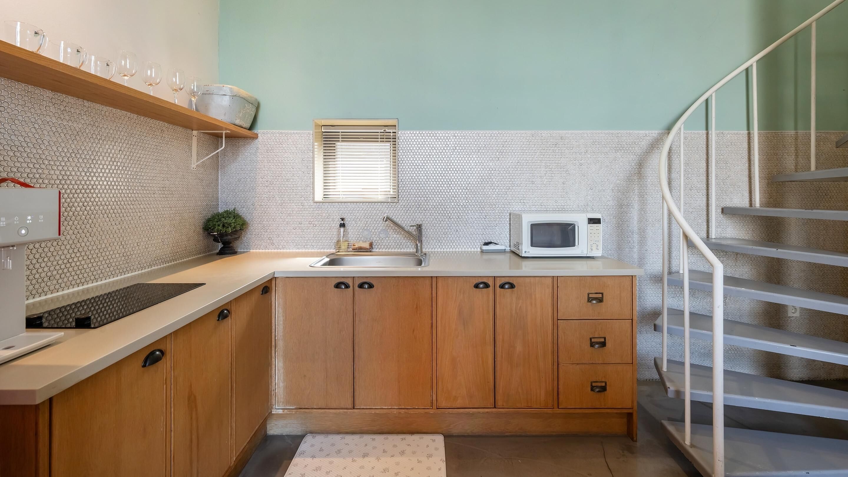 A compact kitchen with wooden cabinets, a stainless steel sink, a microwave, and a small window.