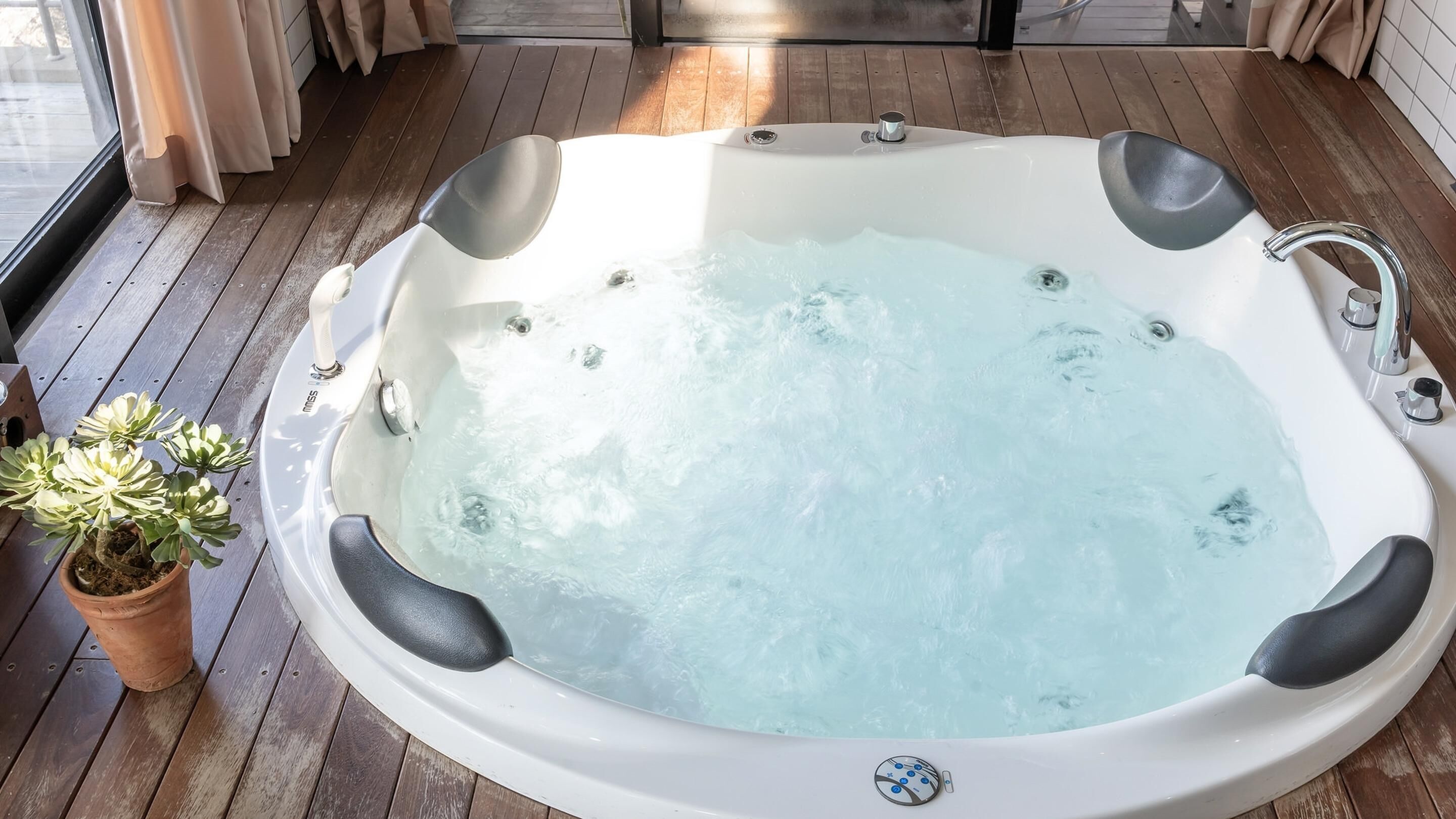 A hot tub with a built-in seat and controls, surrounded by wooden decking and a potted plant.