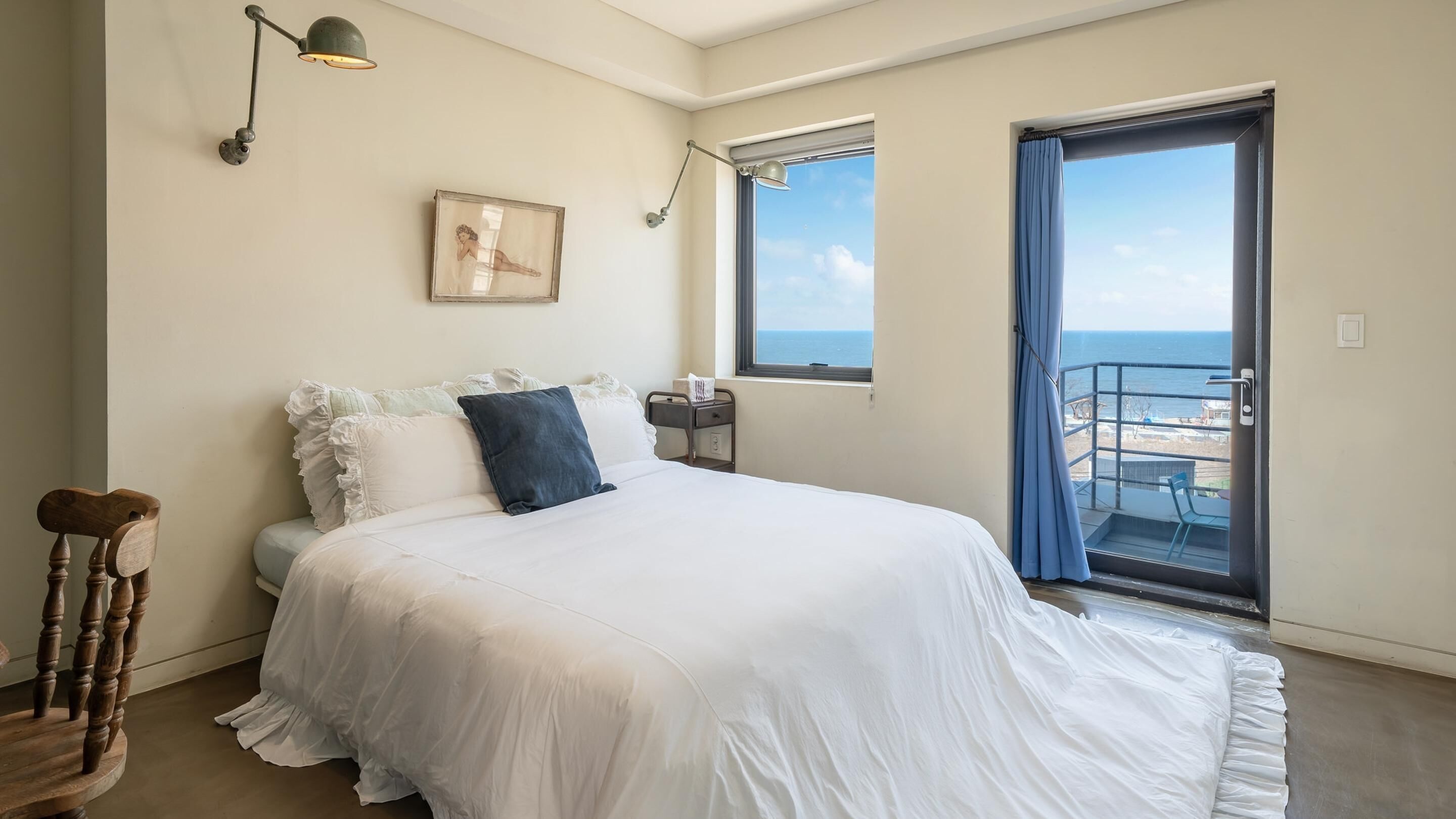 Une chambre à coucher avec un lit, une table de chevet, un tableau encadré et une fenêtre donnant sur la mer.