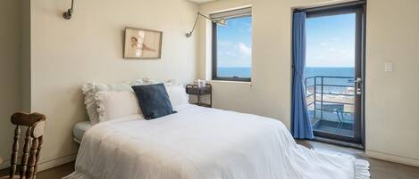 Une chambre à coucher avec un lit, une table de chevet, un tableau encadré et une fenêtre donnant sur la mer.
