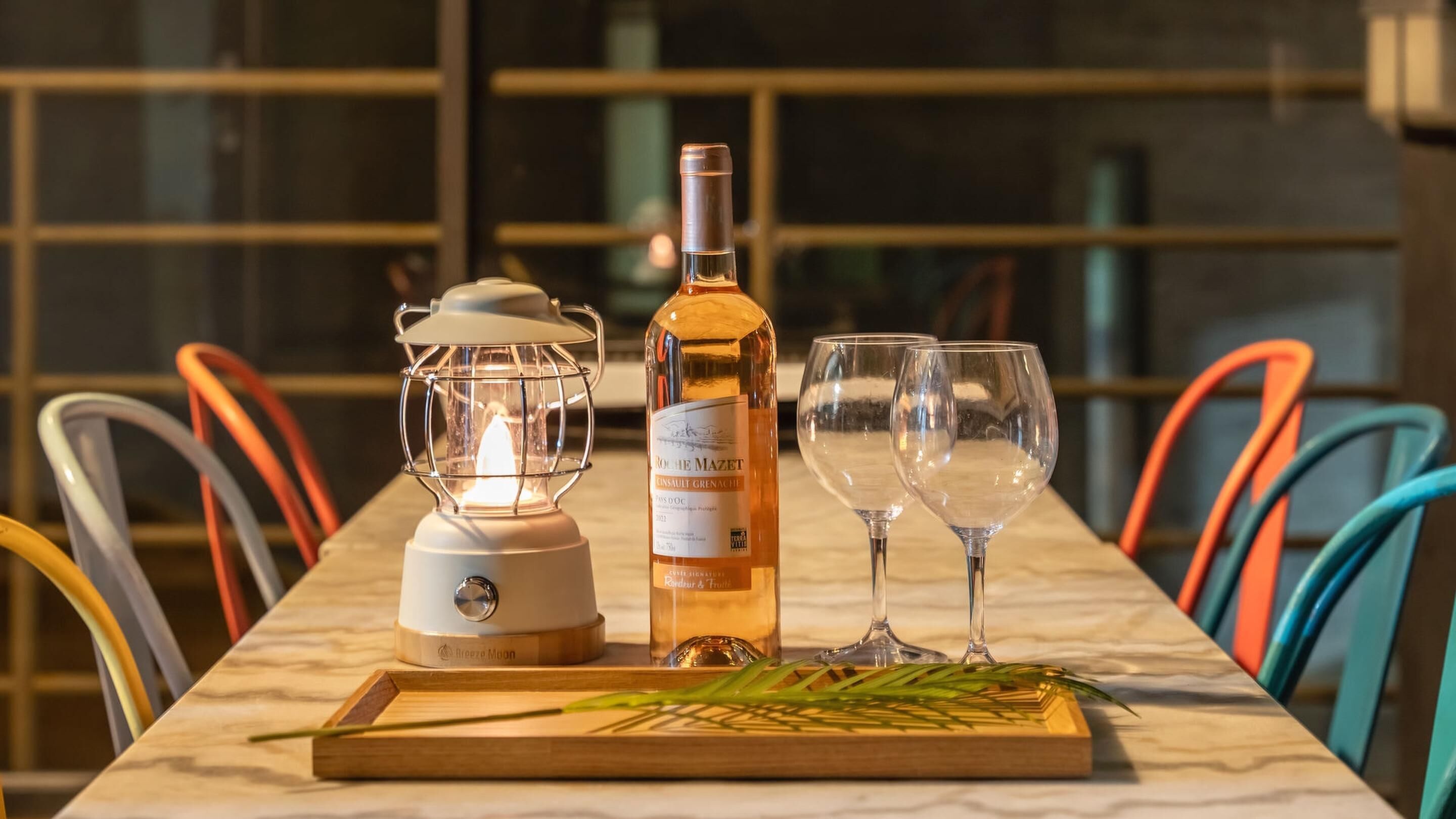 A table with a bottle of wine, two glasses, a blender, and a tray with a plant.
