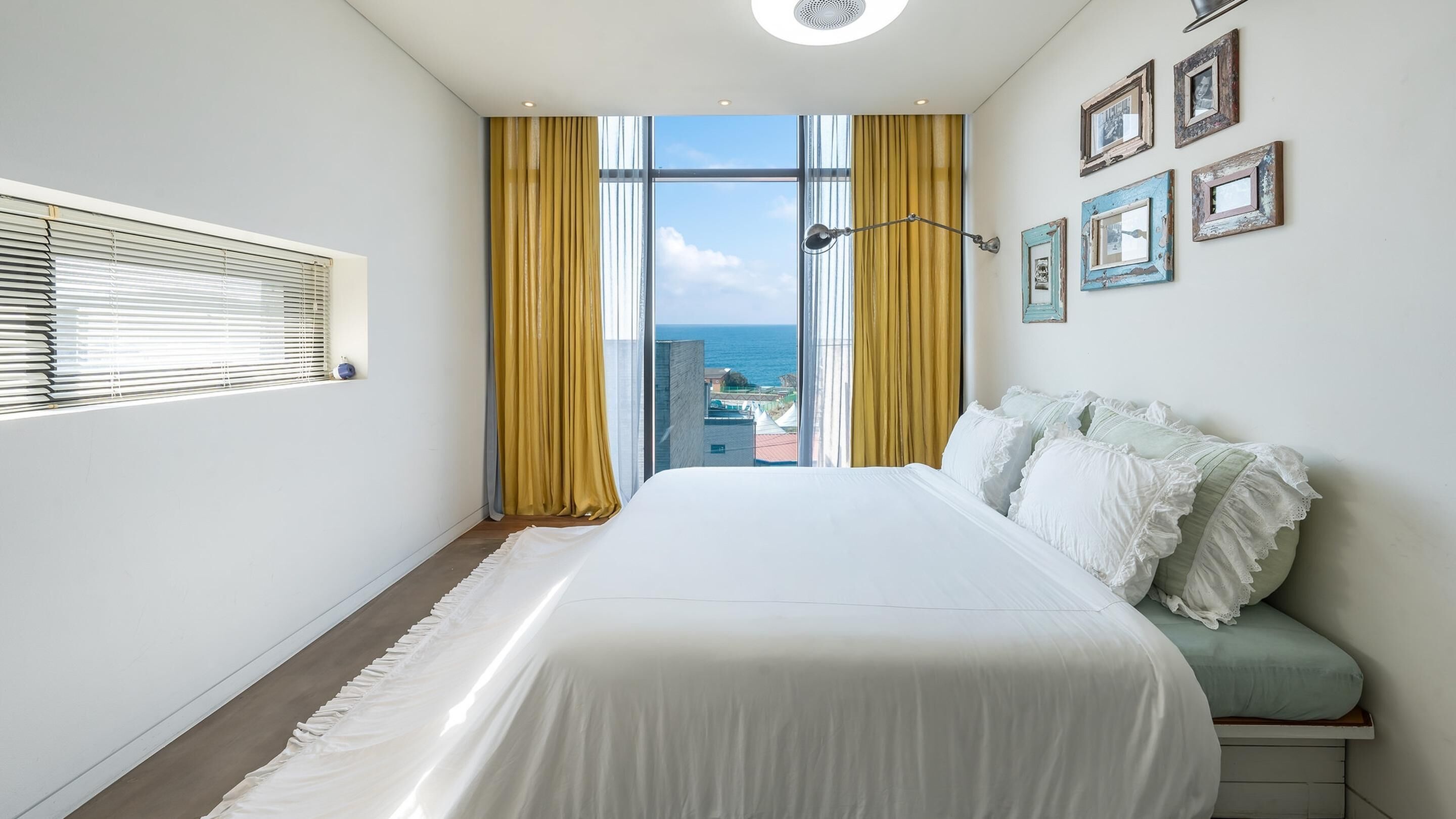A hotel room with a large bed, a view of the sea, and a window with curtains.