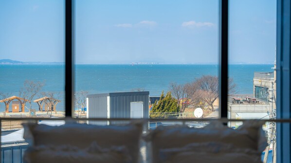 Une vue à travers une fenêtre, avec un ciel dégagé et une étendue d’eau à l’horizon.