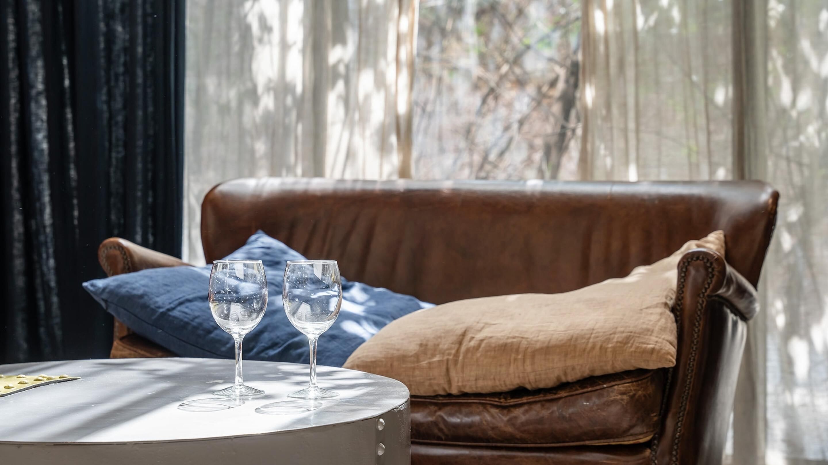 A leather armchair with a cushion, two glasses on a small table, and a window with curtains.