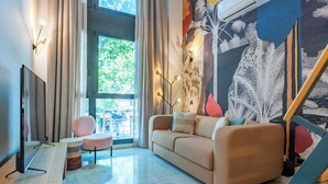 A modern living room with a sofa, a TV, and a dining table. There is a window with curtains and a view of the outdoors. - Smartr Madrid Las Ventas  (Madrid)