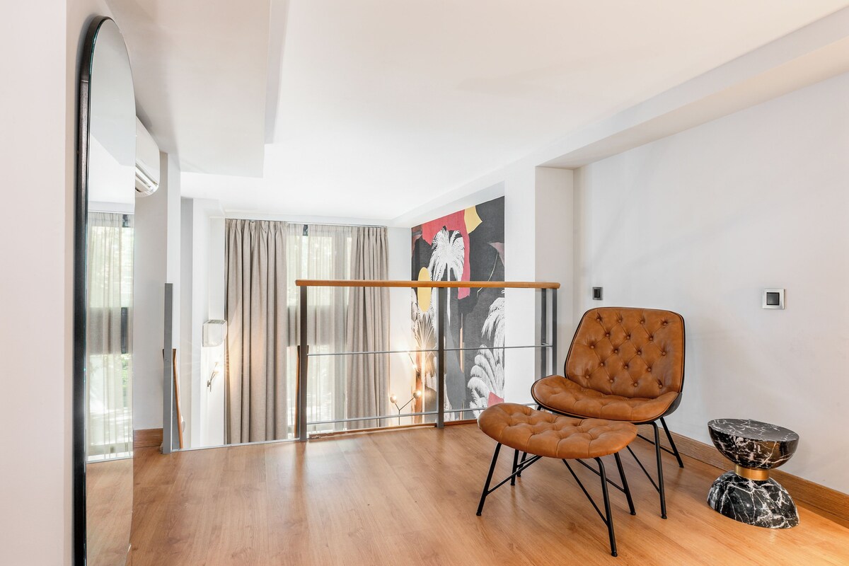 A spacious room with a wooden floor, a brown tufted chair, a small marble side table, and a large mirror.