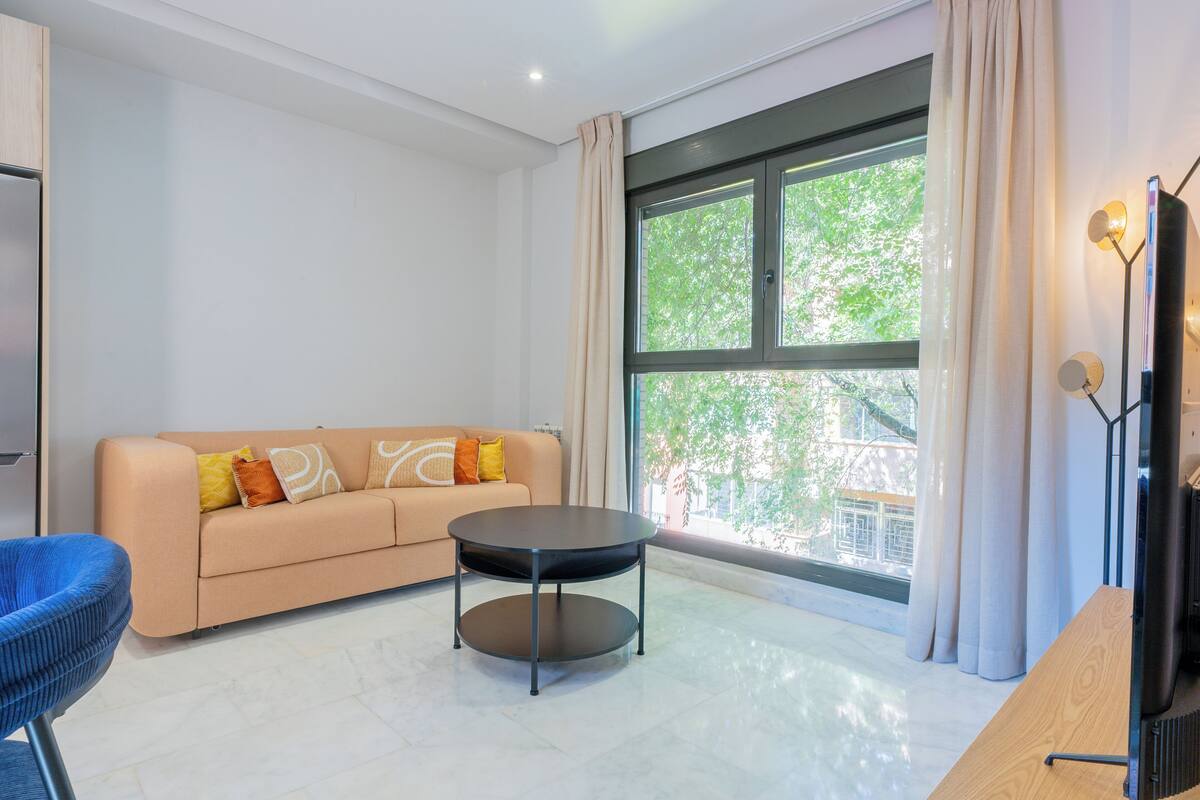 A modern living room with a beige sofa, a round black coffee table, and a blue chair.