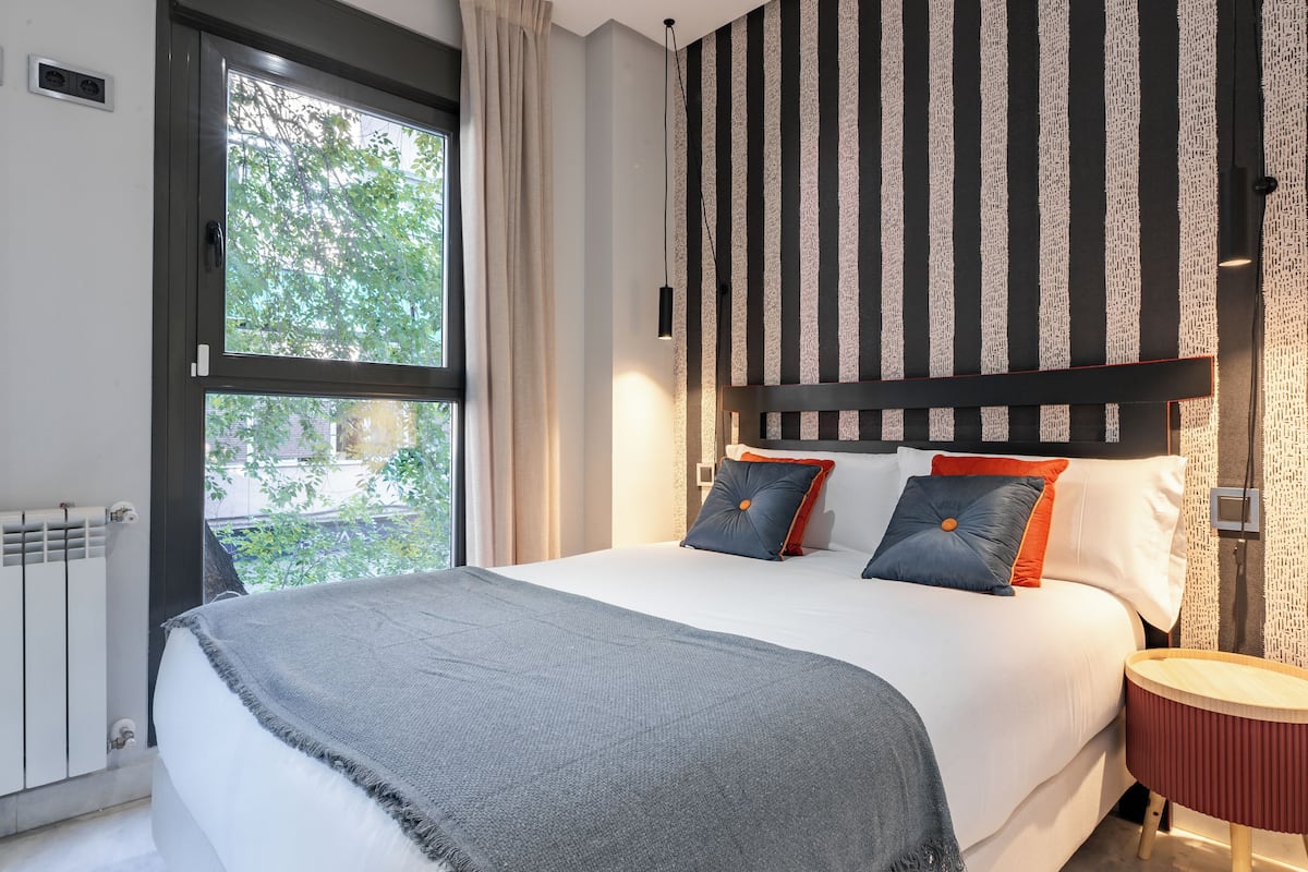 A bedroom with a large bed, a window, a radiator, and striped wallpaper.