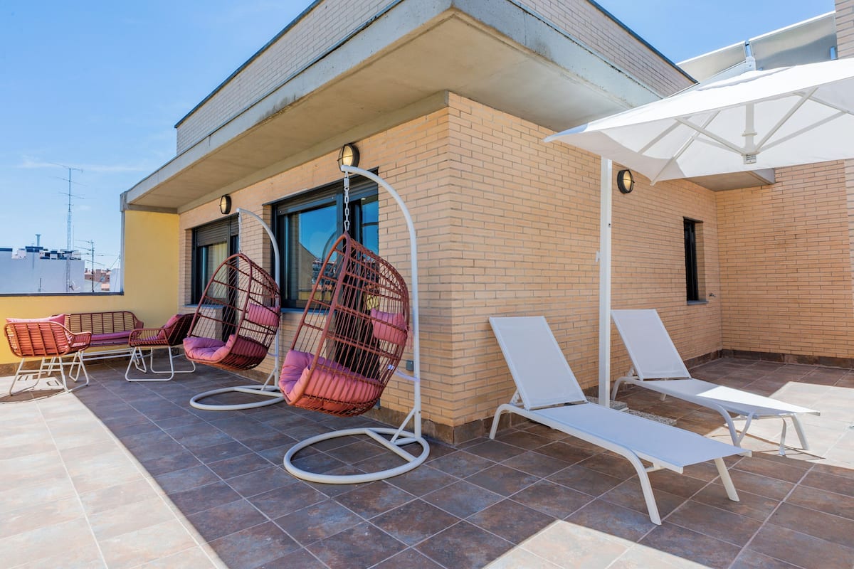 A rooftop terrace with hanging chairs, lounge chairs, and a white umbrella.