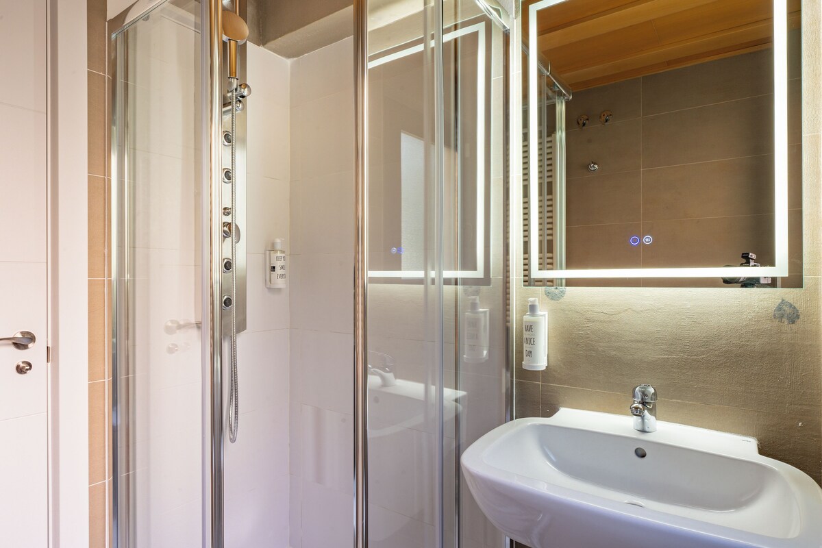 A bathroom with a glass shower enclosure, a white sink, and a mirror above the sink.