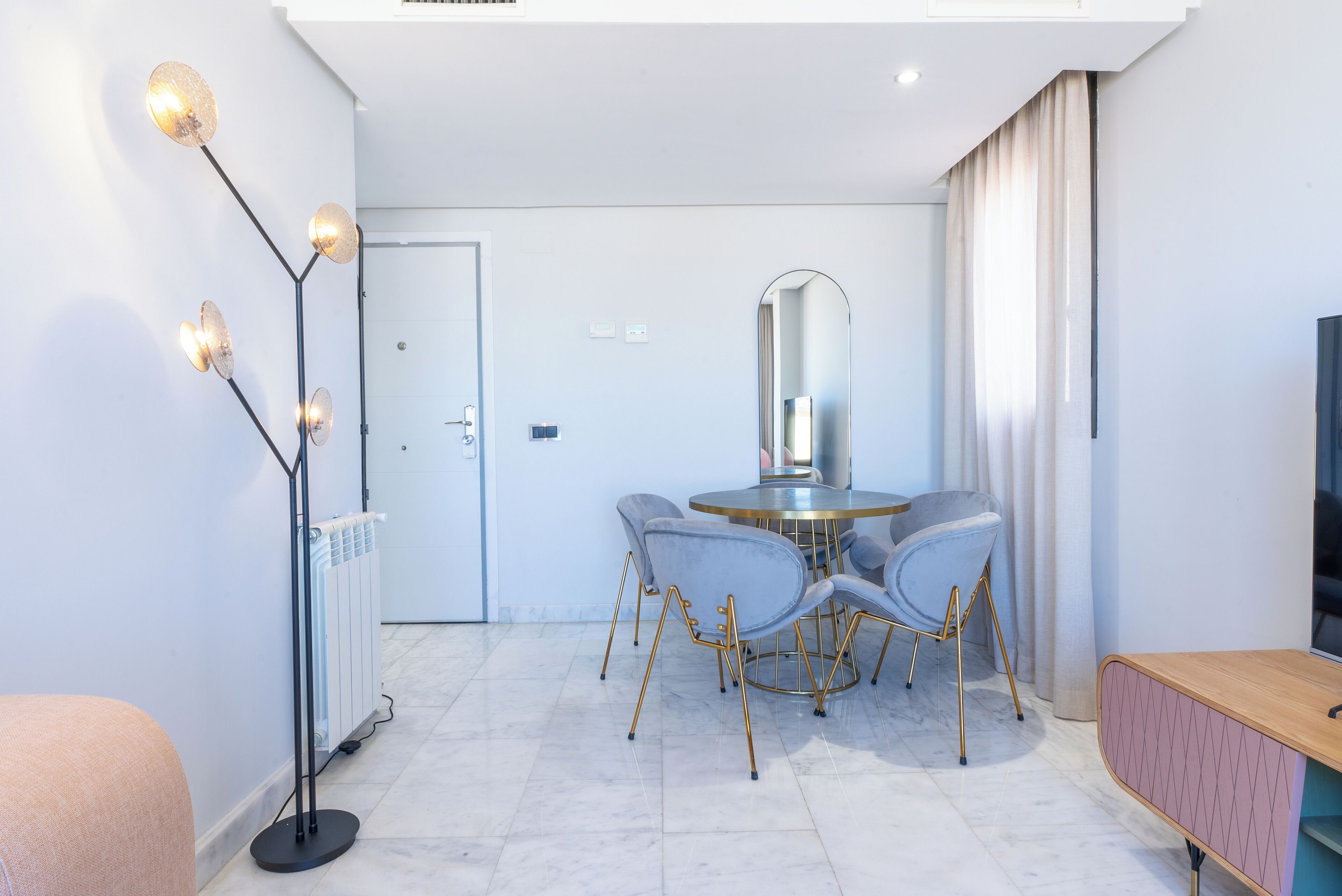 A modern dining area with a round table, grey upholstered chairs, and a floor lamp with multiple light bulbs.