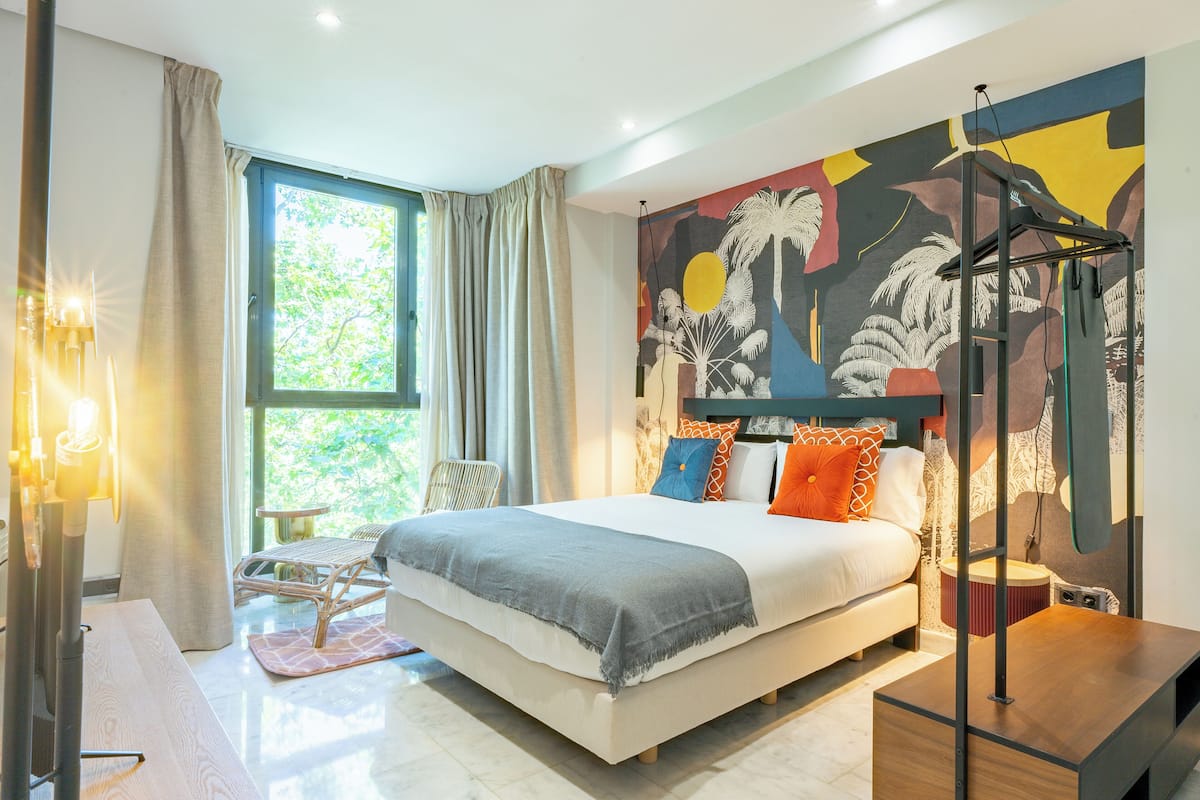 A modern bedroom with a large bed, a wall mural, and a window with curtains.