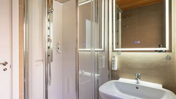 A bathroom with a glass shower enclosure, a white sink, and a mirror above the sink.