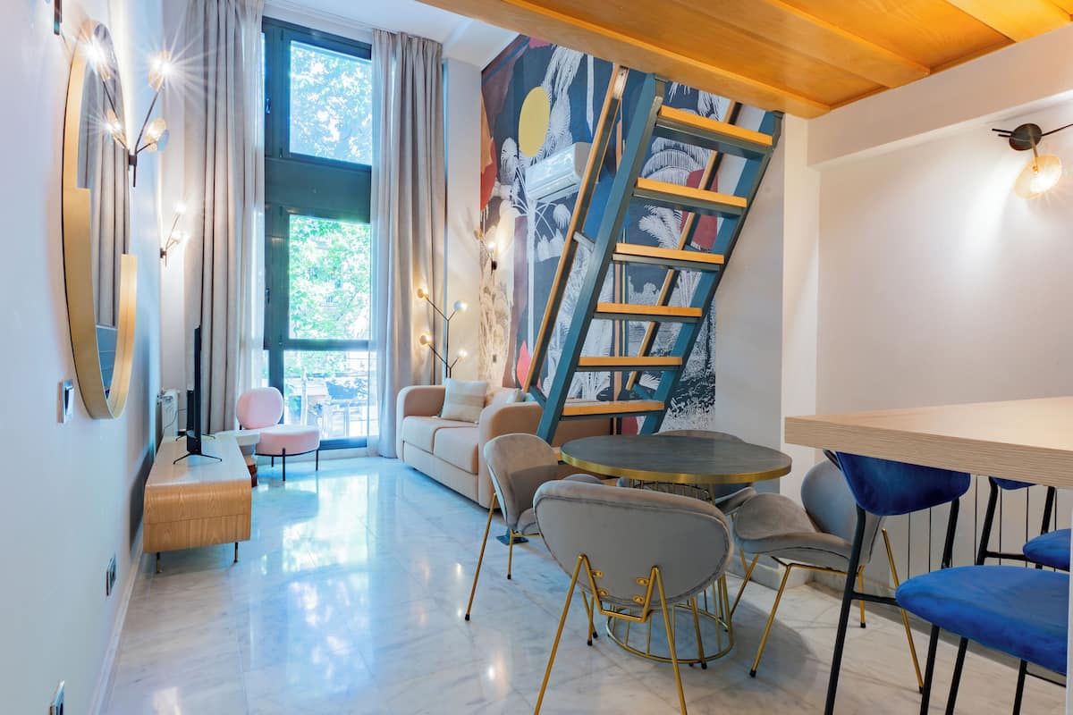 A modern living room with a sofa, chairs, a round table, and a staircase.