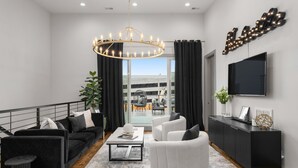 A modern living room with a black and white sofa set, a coffee table, a chandelier, a TV, and a balcony view. - Luxe Getaway with Hot Tub (Nashville)