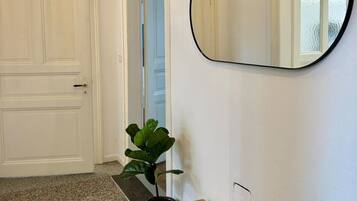 Een gang met een witte deur, een ronde spiegel, een houten bankje en een plant.