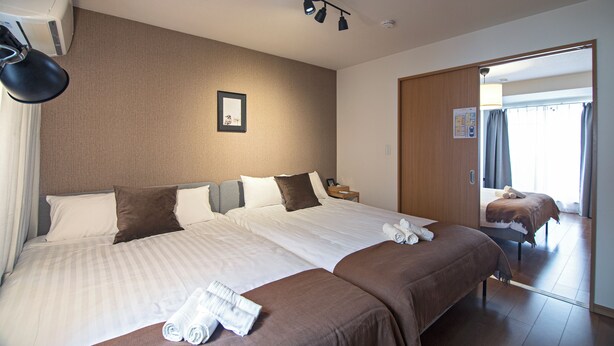 A hotel room with two beds, a large mirror, and a ceiling-mounted light fixture. - Hayashitera 2LDK 6ppl  (Osaka)