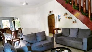 A living room with two grey sofas, a coffee table, and a dining area with wooden furniture. - La Source Self Catering (La Digue)
