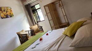 A bedroom with a bed, a wooden ceiling, an air conditioning unit, a window, and a wooden wardrobe. - La Source Self Catering (La Digue)