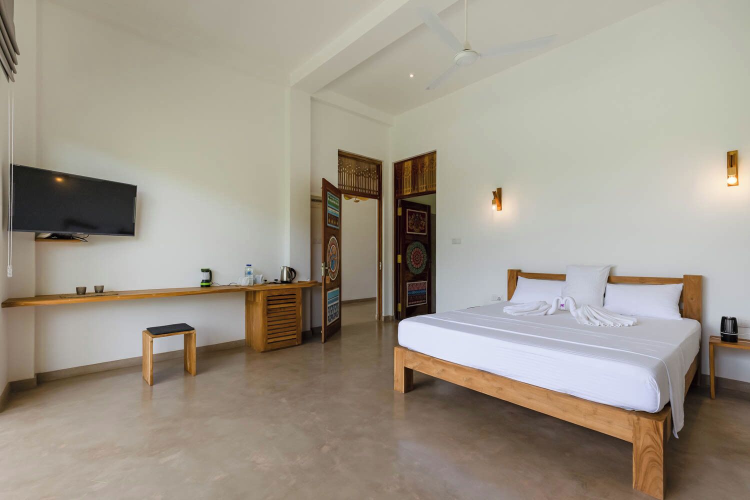 Una camera d'albergo con un letto, una scrivania, una televisione e una porta che dà su un'altra stanza.