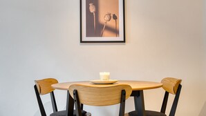 A dining area with a round table, two wooden chairs, and a framed picture of poppies on the wall.
