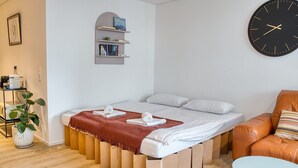 A modern bedroom with a bed, a clock, a bookshelf, a coffee machine, and a plant.