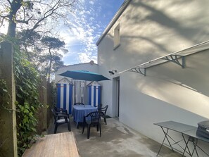 Une terrasse avec une table et des chaises, une petite table et un parasol bleu.