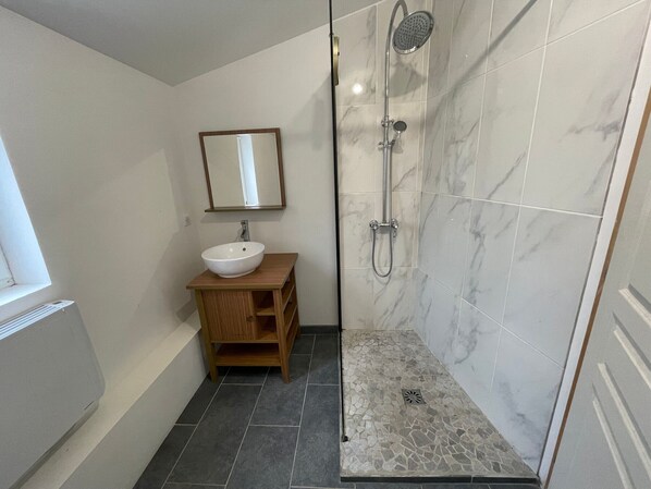 A bathroom with a white sink, wooden vanity, a mirror, a shower with a handheld showerhead, and marble tiles.