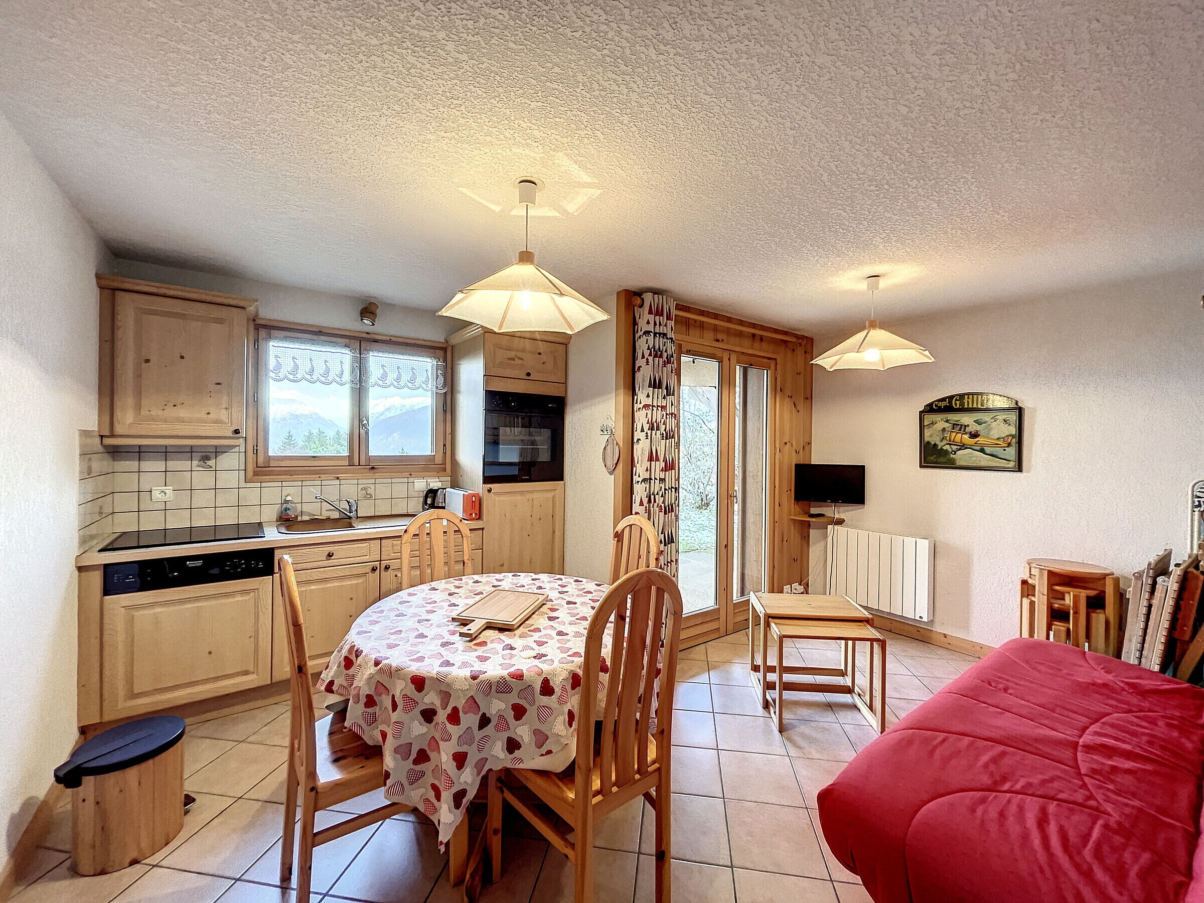 A cozy kitchen with wooden cabinets, a dining table with a floral tablecloth, and a red sofa.