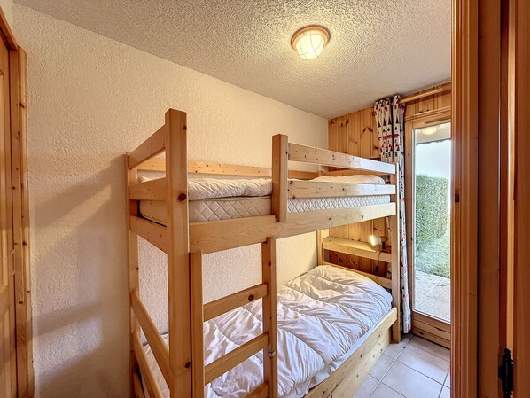 A bunk bed room with a wooden ceiling and a window with curtains. - Cozy 2BR Apartment with Garden, Near Ski Bus & Village (Combloux)