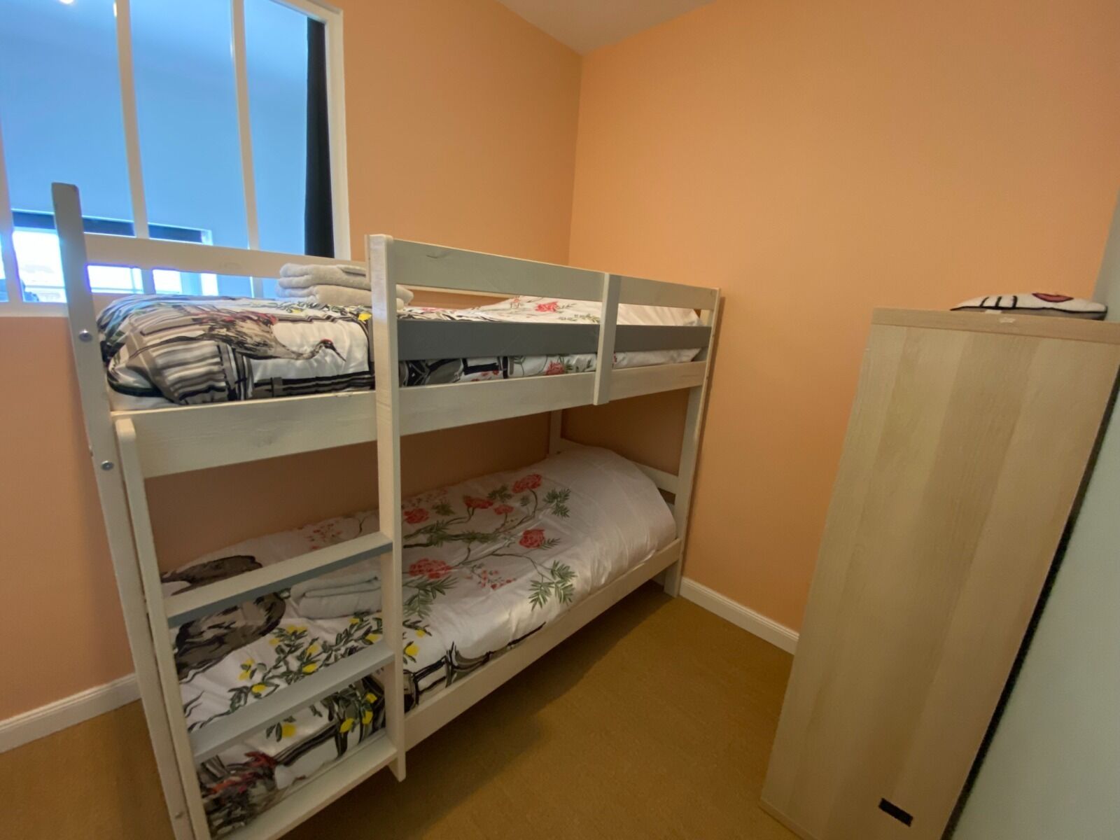 Un letto a castello con scaffali contenitori, un armadio e una finestra in una stanza dalle pareti color pesca.