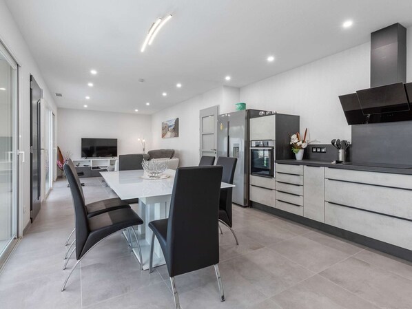 A modern kitchen with a dining area, a built-in oven, and a large window.