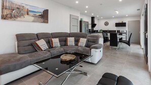 A modern living room with a sectional sofa, a glass coffee table, and a dining area with a kitchen in the background.