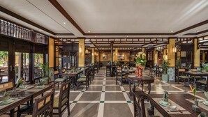 Un espaiós restaurant amb taules i cadires de fusta, un sòl amb ratlles de quadradets i plantes decoratives.