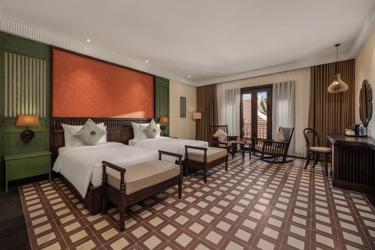 Ein Hotelzimmer mit zwei Betten, einer Sitzecke und Blick durch ein Fenster nach draußen.