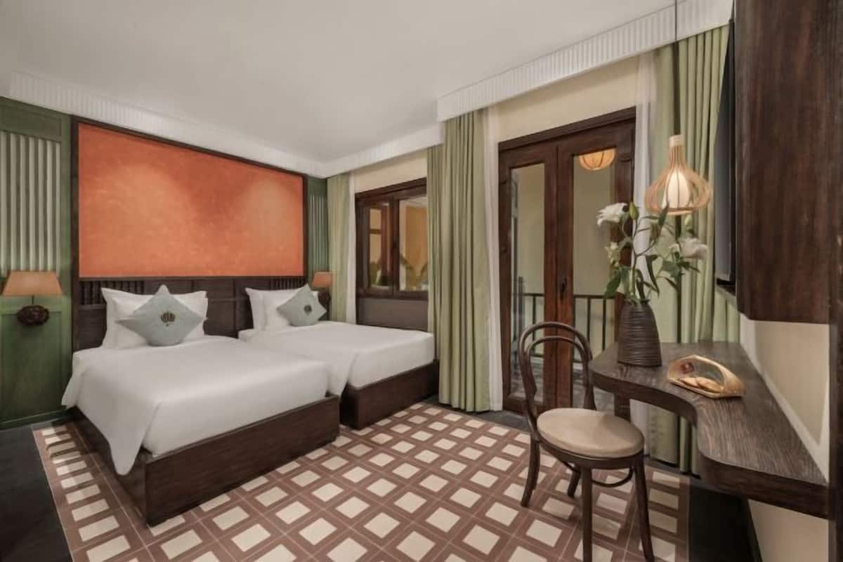 Ein Hotelzimmer mit zwei Betten, einem Schreibtisch, einem Stuhl, einem Spiegel und einem großen Fenster.