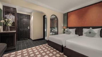 A hotel room with two beds, a wooden wardrobe, a tiled floor, and a view through an arched doorway.