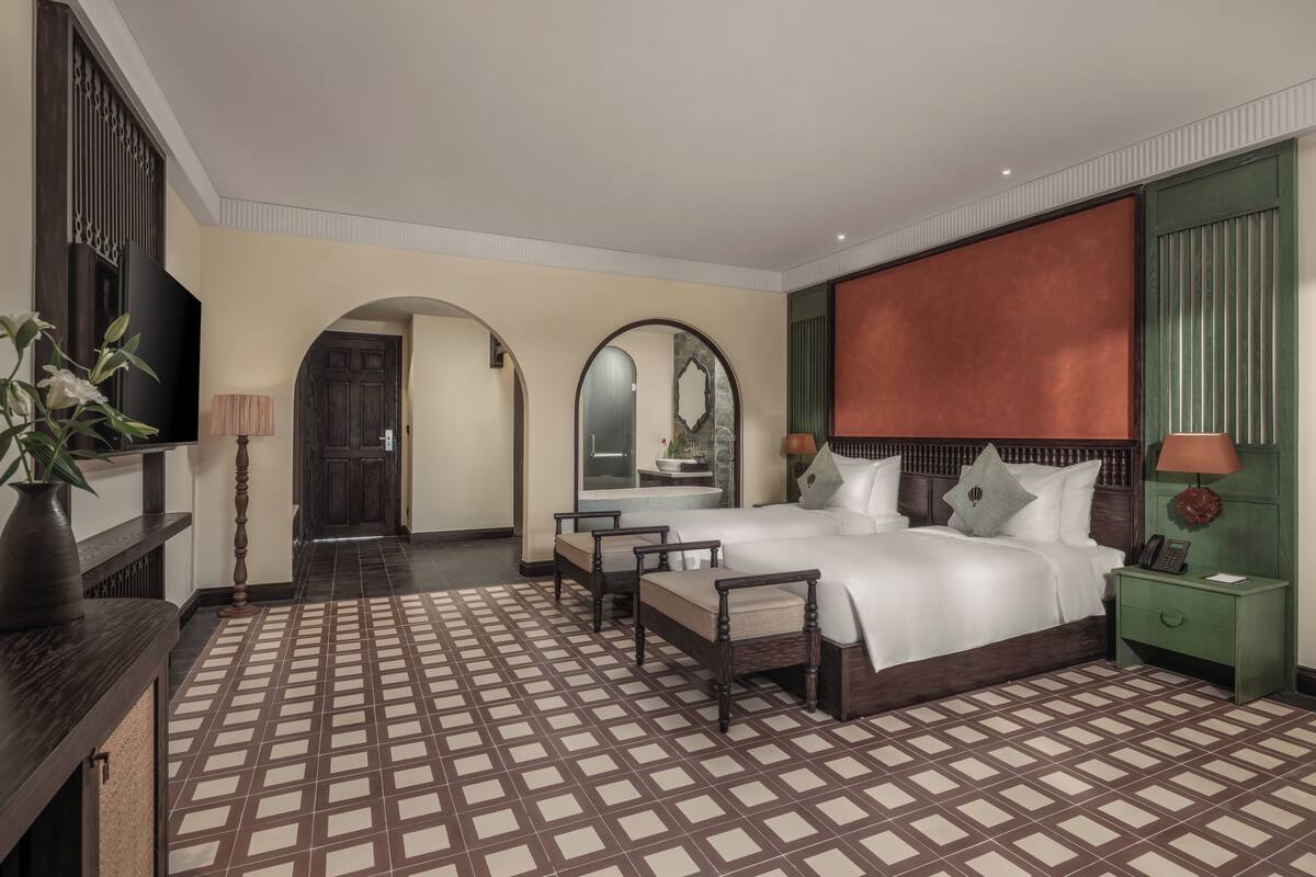 Ein Hotelzimmer mit einem großen Bett, zwei Nachttischen, einem Fernseher, einem Schreibtisch mit Lampe und einem gemusterten Boden.